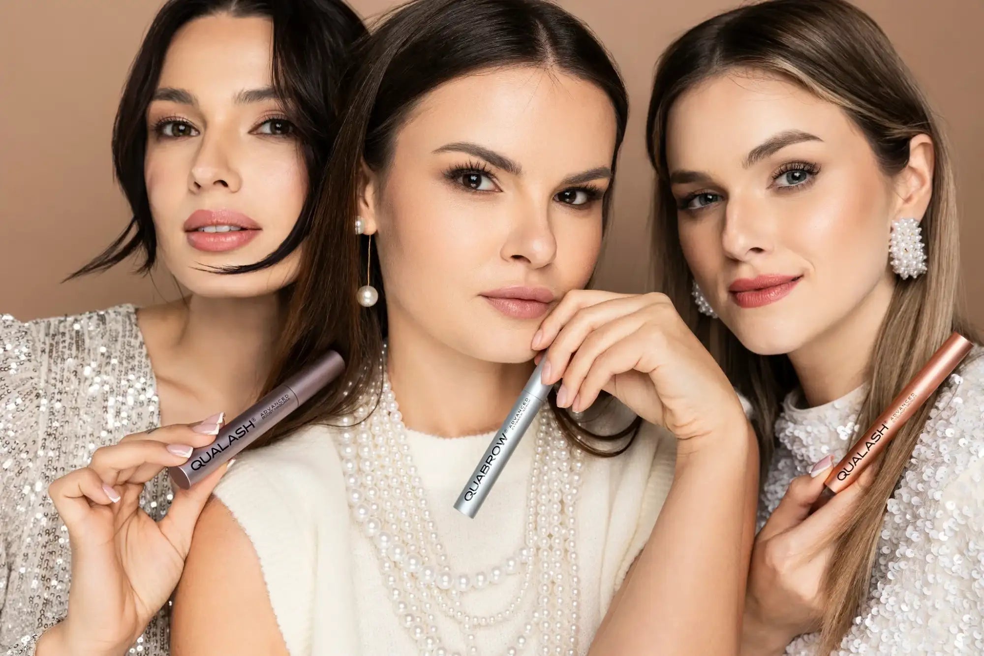 Beauty editorial image of three women holding Qualash eyelash serum, lash mascara and Quabrow eyebrow serum on a neutral background
